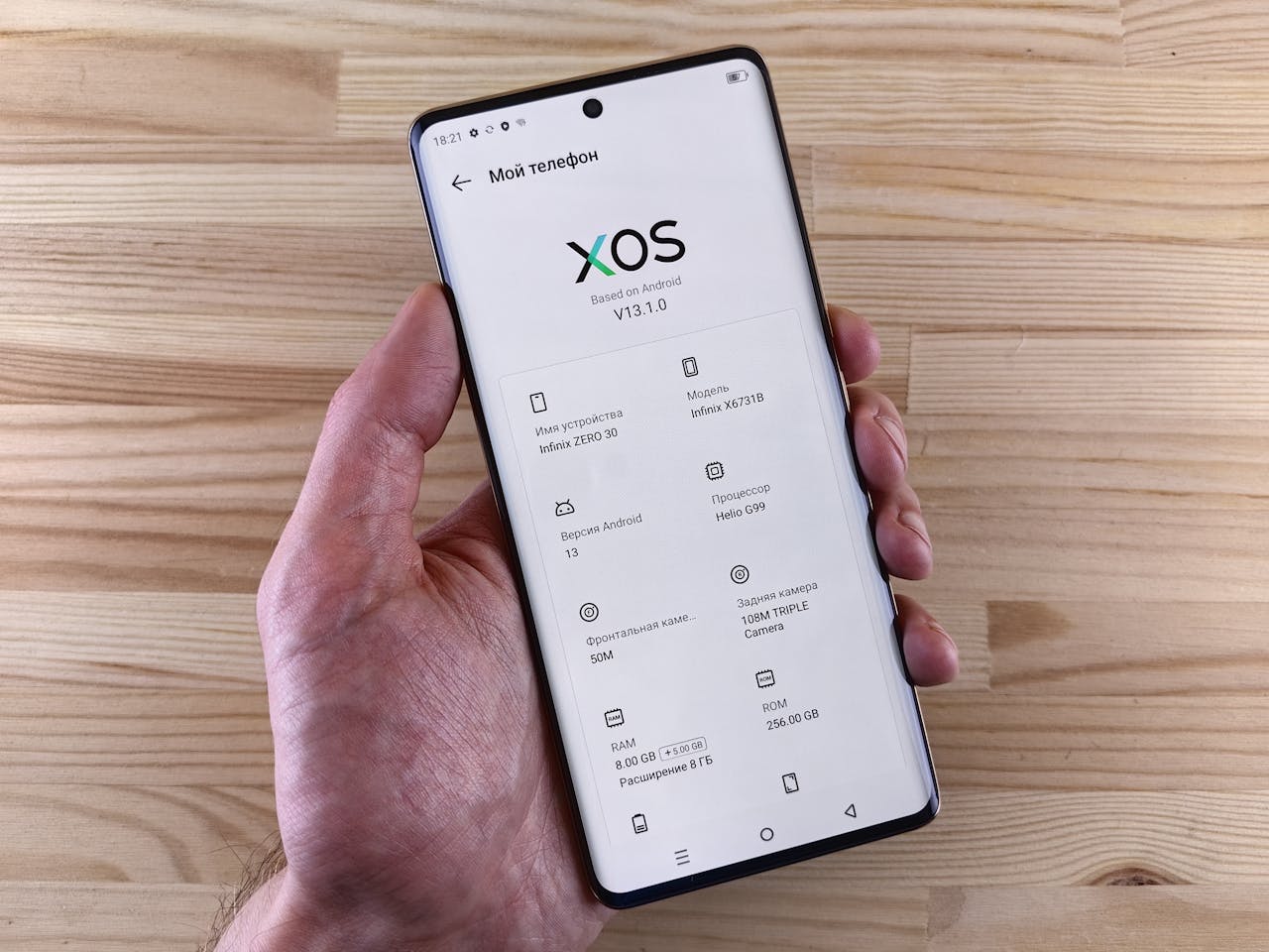 Close-up of a hand holding a smartphone displaying the XOS interface with specs.